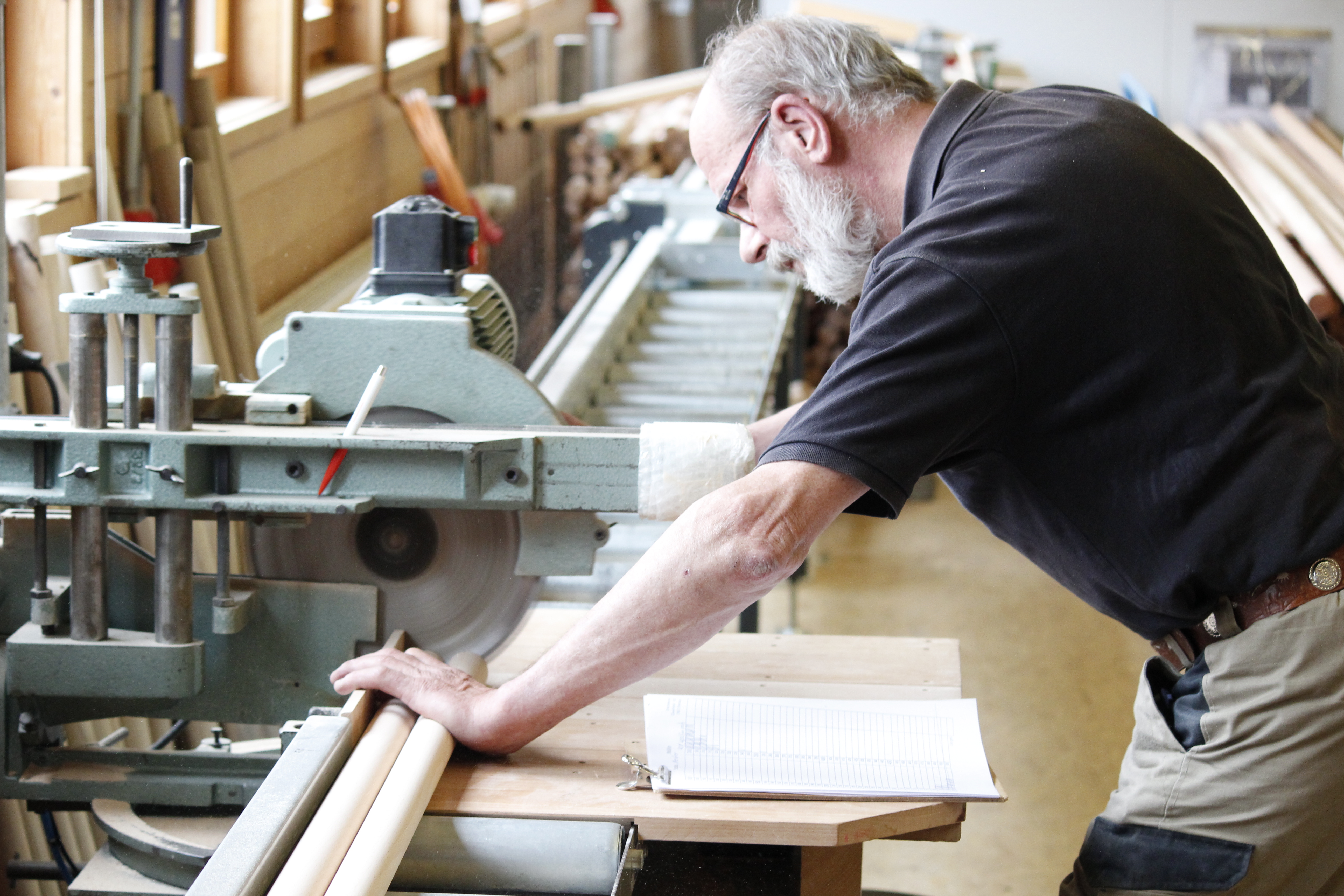Fabrication de mains courantes : employé alignant des mains courantes en bois à la scie à onglet, bloc-notes sur l'établi