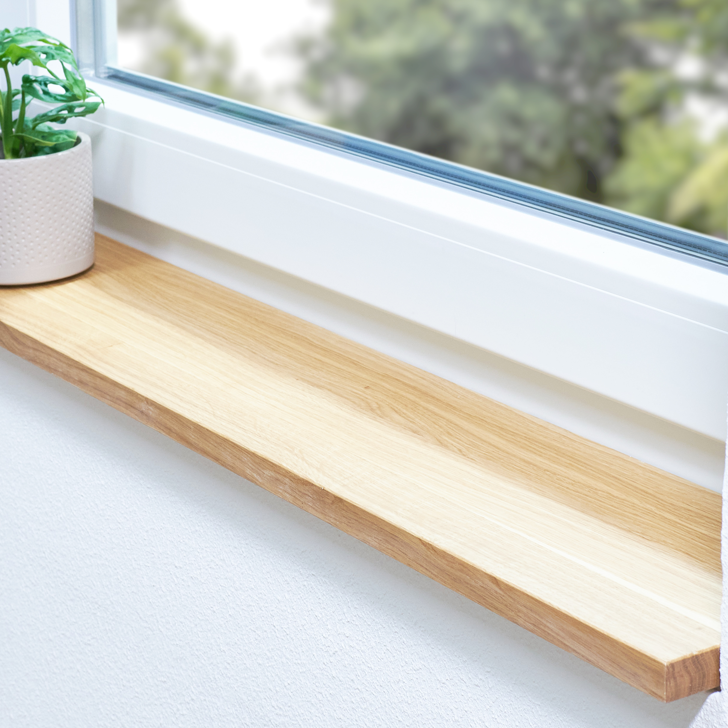 Appui de fenêtre en chêne naturel, lamelles continues, dans une embrasure blanche avec plante en pot et vue sur la verdure