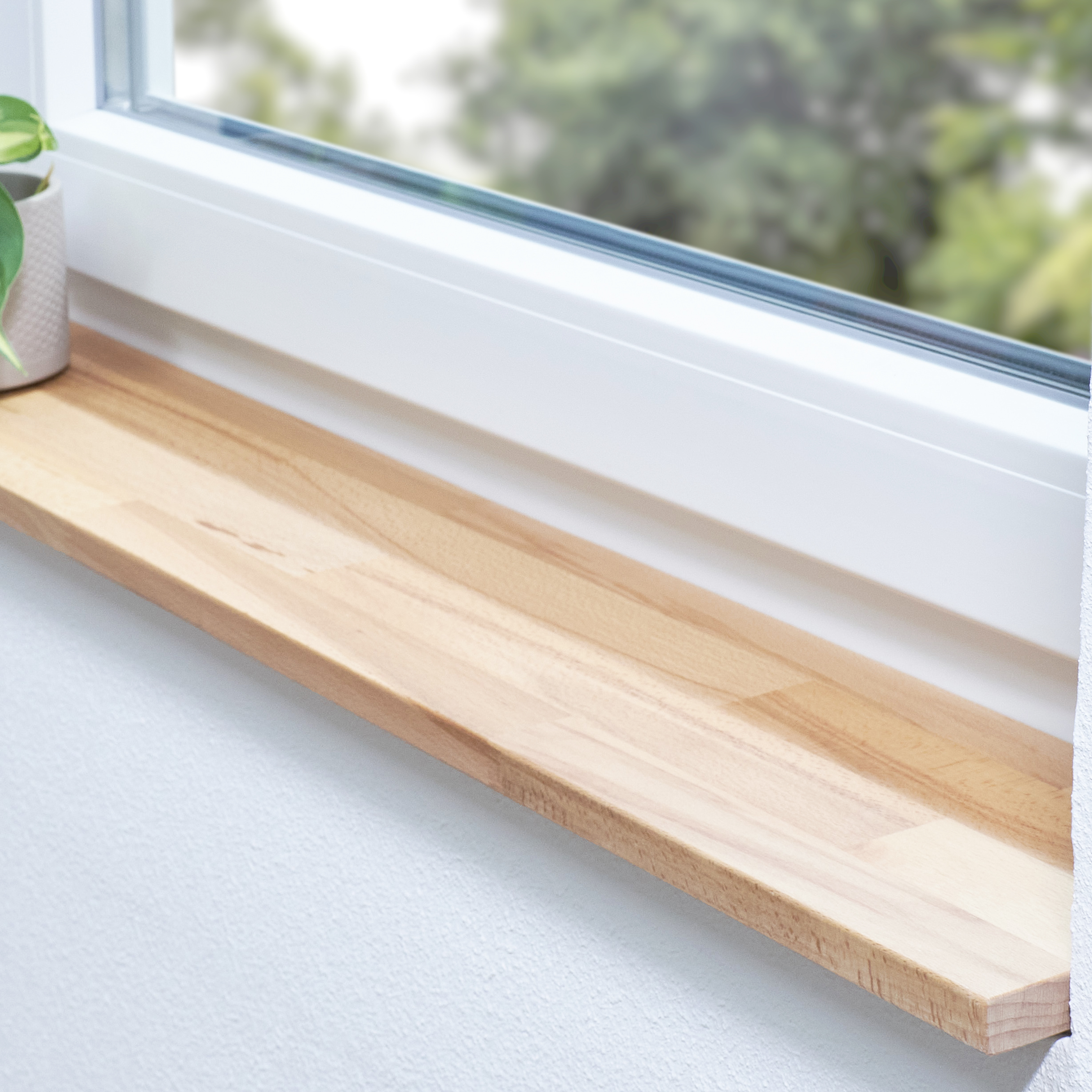 Appui de fenêtre en hêtre à cœur rouge naturel, abouté, dans une embrasure blanche avec plante et vue sur la verdure