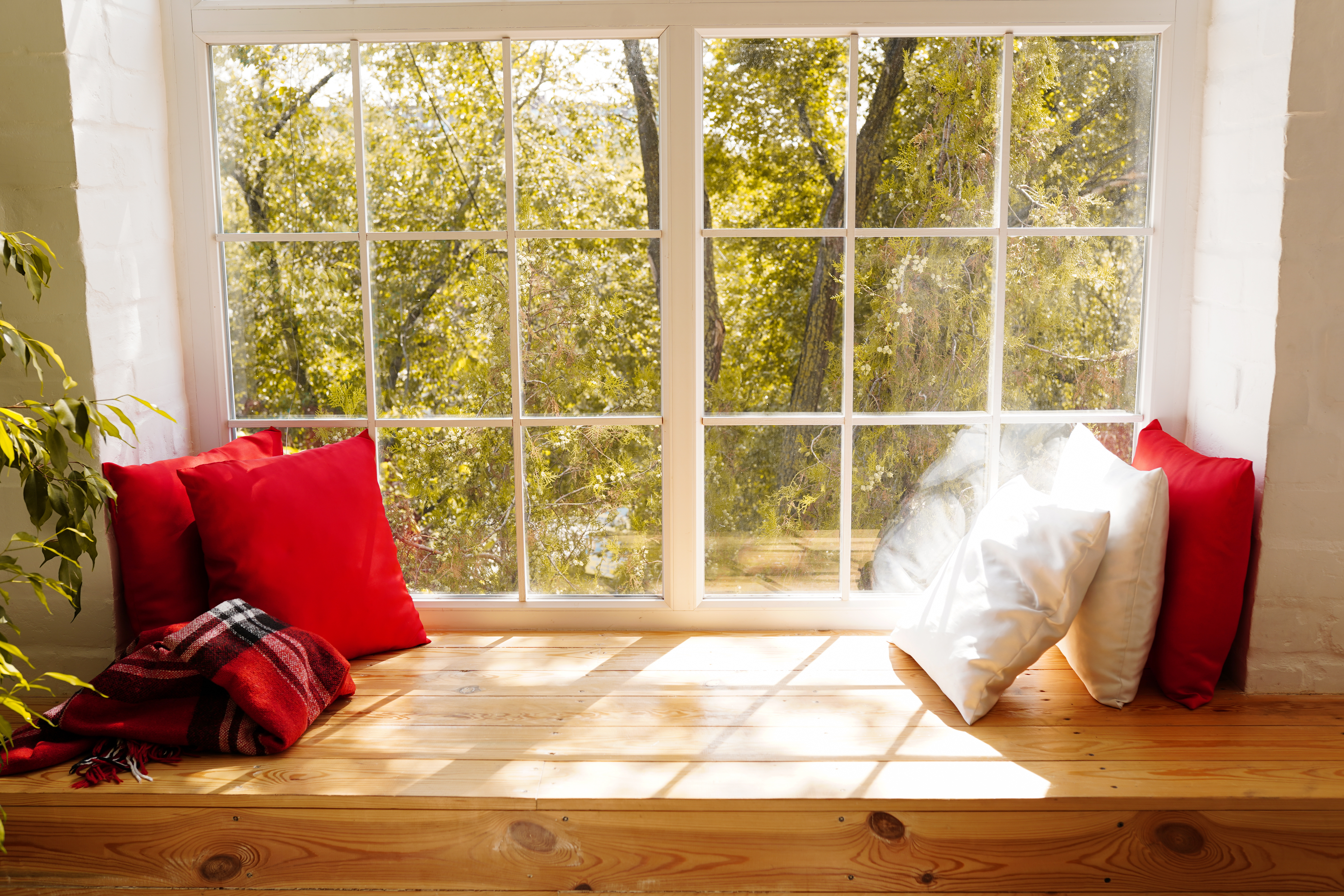 Appui de fenêtre large en bois massif servant de banquette, coussins rouges et blancs devant fenêtre à petits bois