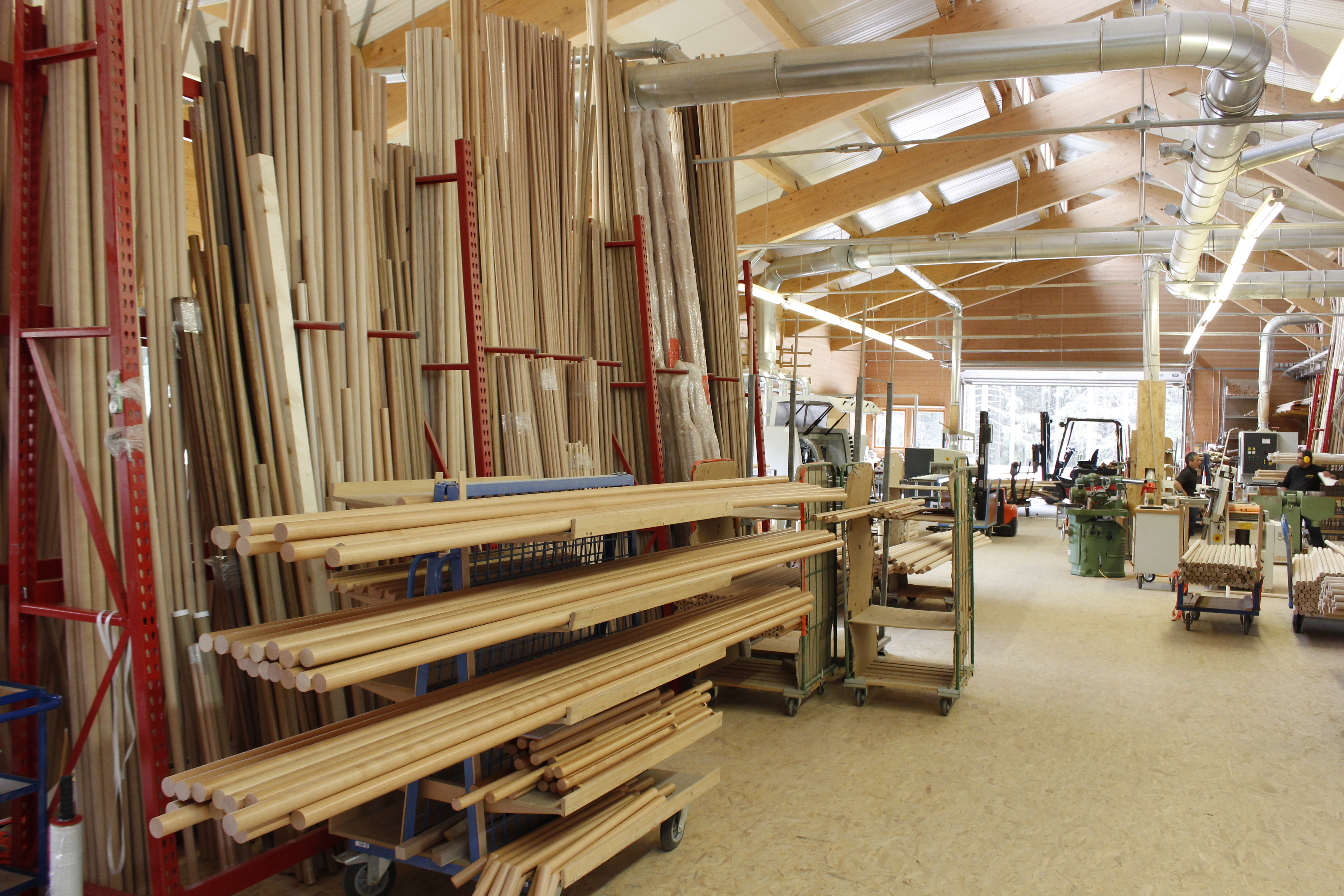 Mains courantes en bois et barres rondes dans l'entrepôt de la tournerie, longues barres sur rayonnages cantilever rouges