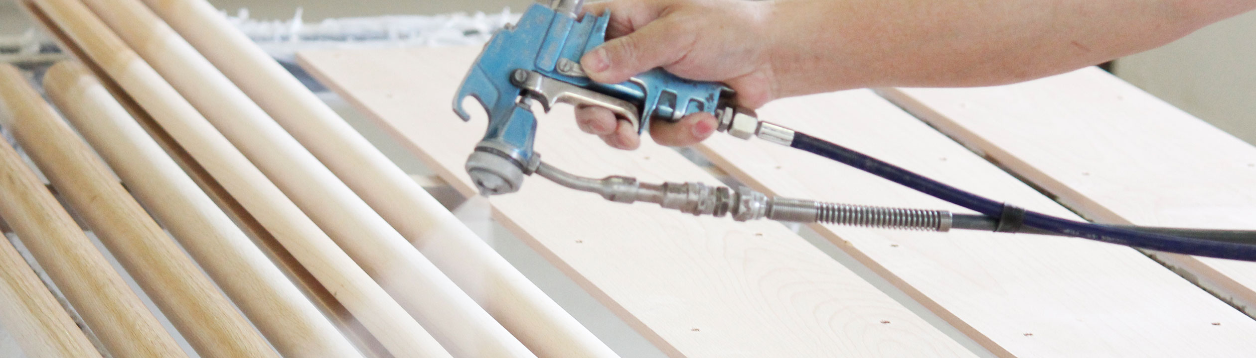 Fabrication de mains courantes : laquage de mains courantes en bois au pistolet, main avec pistolet sur des barres claires