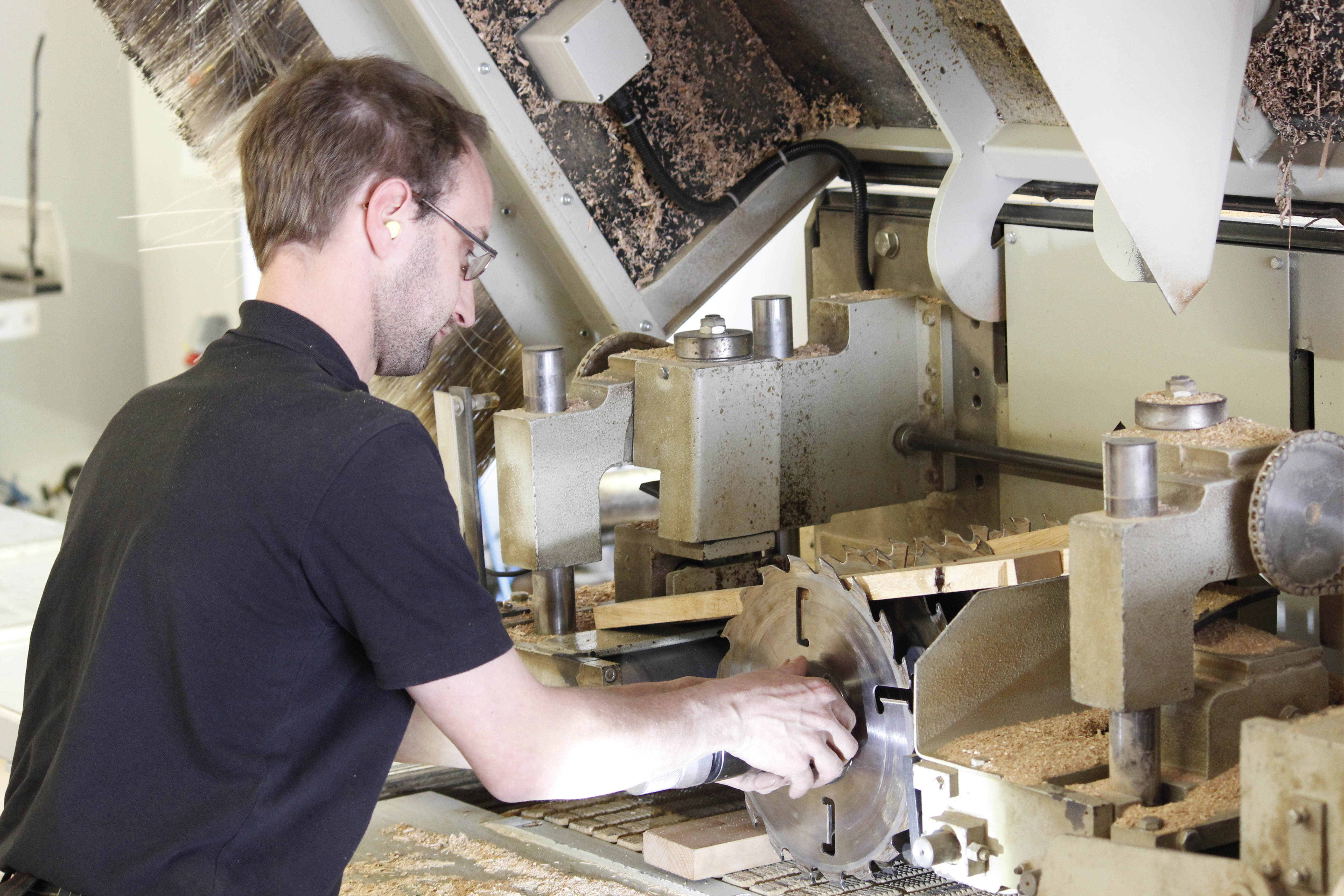 Artisan du bois à une raboteuse dans l'atelier, en train d'usiner du bois massif, copeaux sur la machine