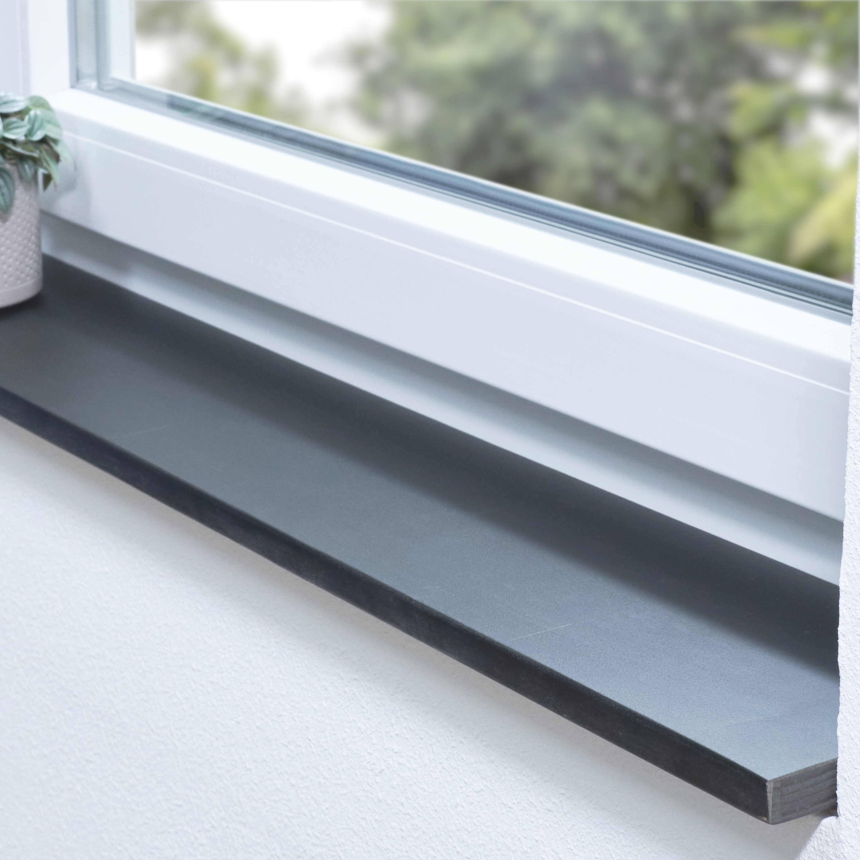 Appui de fenêtre en hêtre à cœur rouge teinté noir, abouté, dans une embrasure blanche avec plante et vue sur la verdure