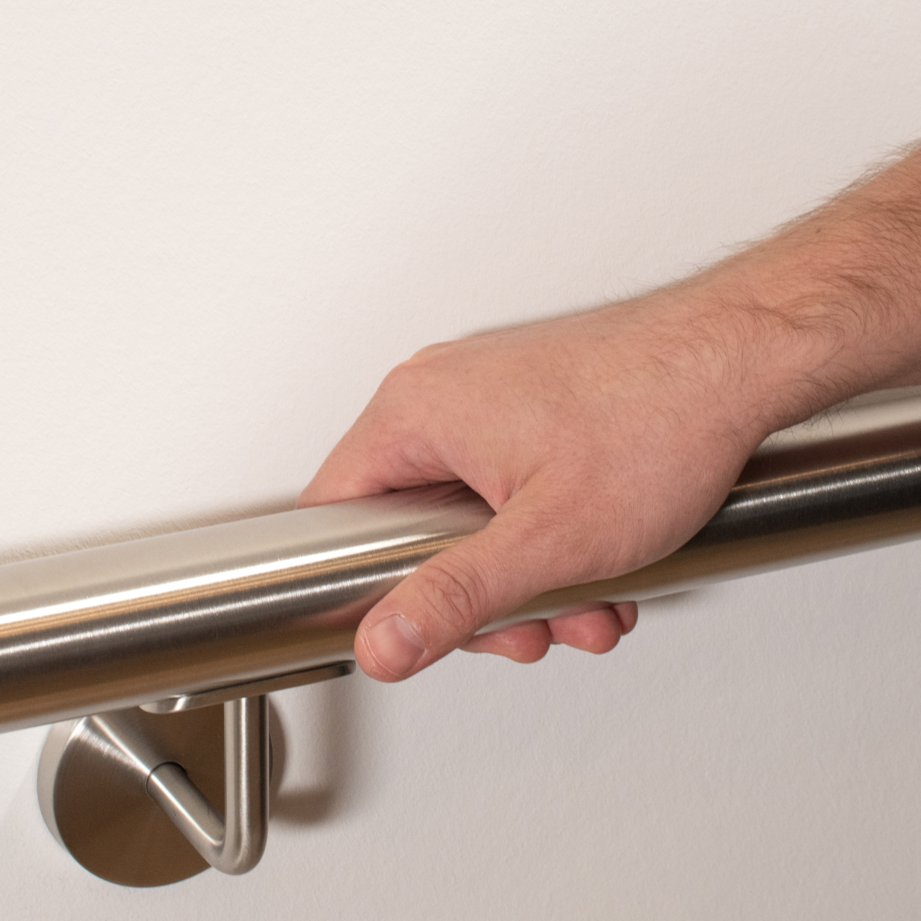 Main courante ronde en acier inoxydable sur mur blanc avec support inox, une main entoure la main courante, gros plan