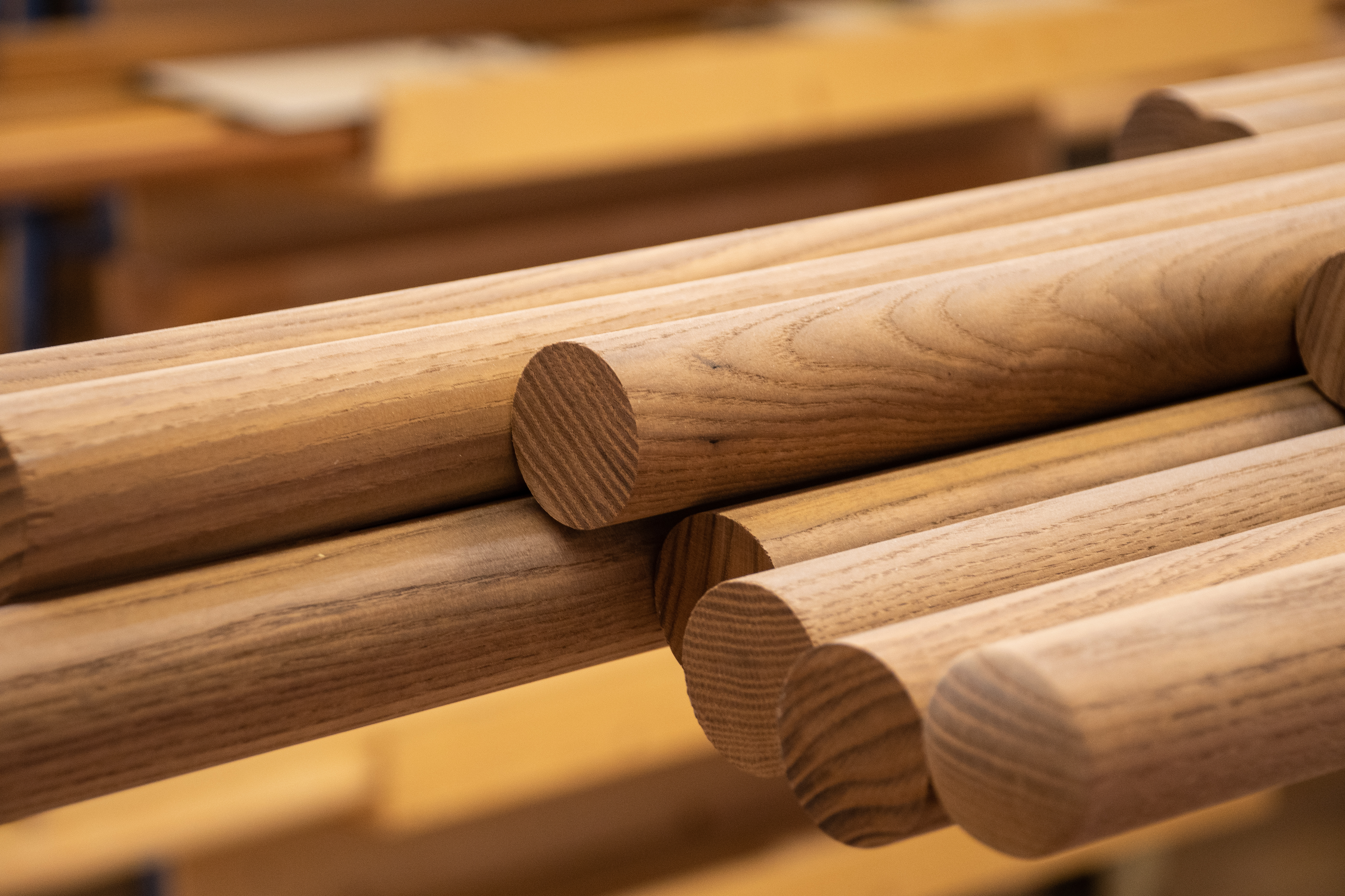 Mains courantes rondes en bois empilées sur l'étagère de l'atelier, abouts et veinage visibles, gros plan