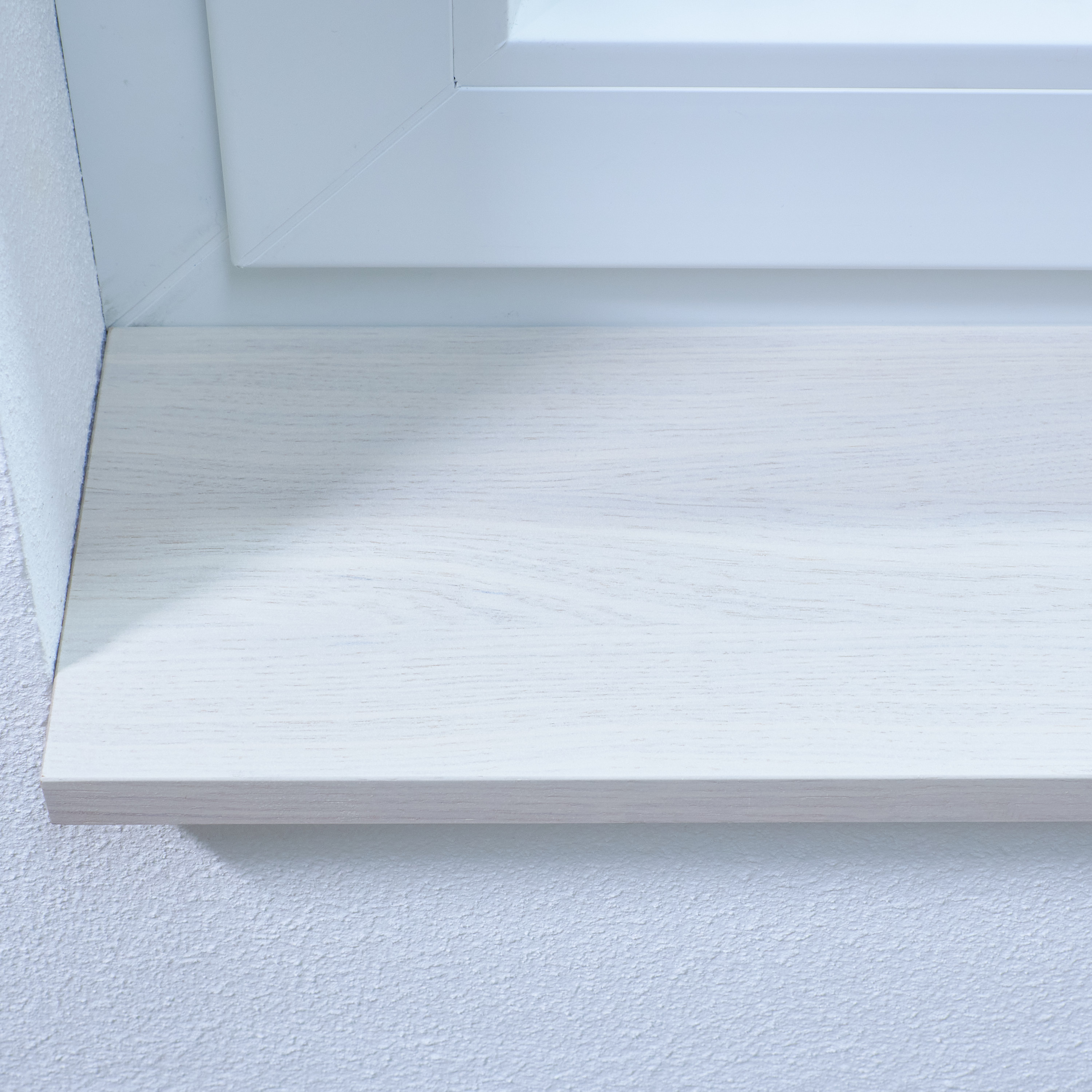 Appui de fenêtre teinté blanc au veinage visible, gros plan sur le chant avant sous un cadre de fenêtre blanc