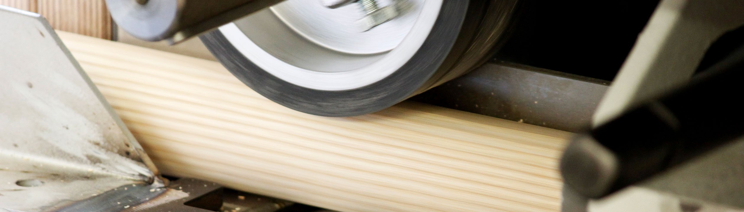 Fabrication de mains courantes : barre ronde en bois poncée dans la ponceuse, gros plan du rouleau de ponçage, bannière