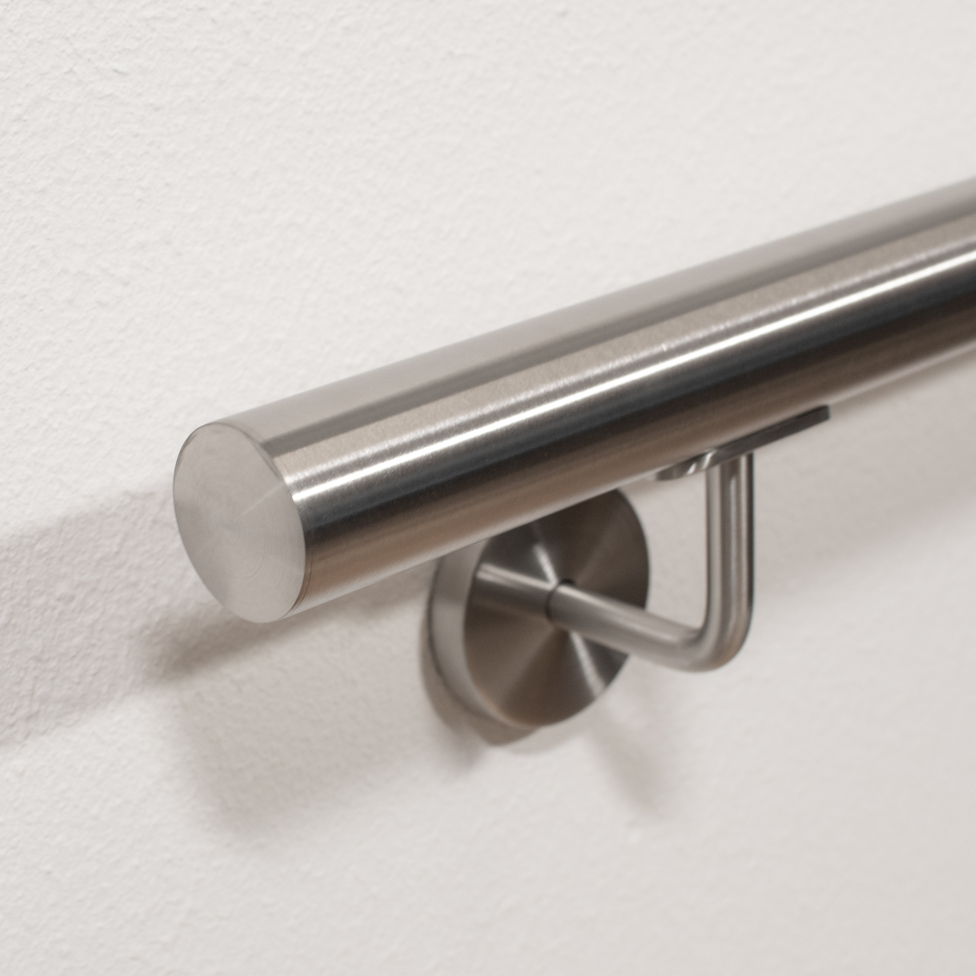 Main courante ronde en acier inoxydable avec support mural et embout plat sur mur blanc, gros plan en contre-plongée