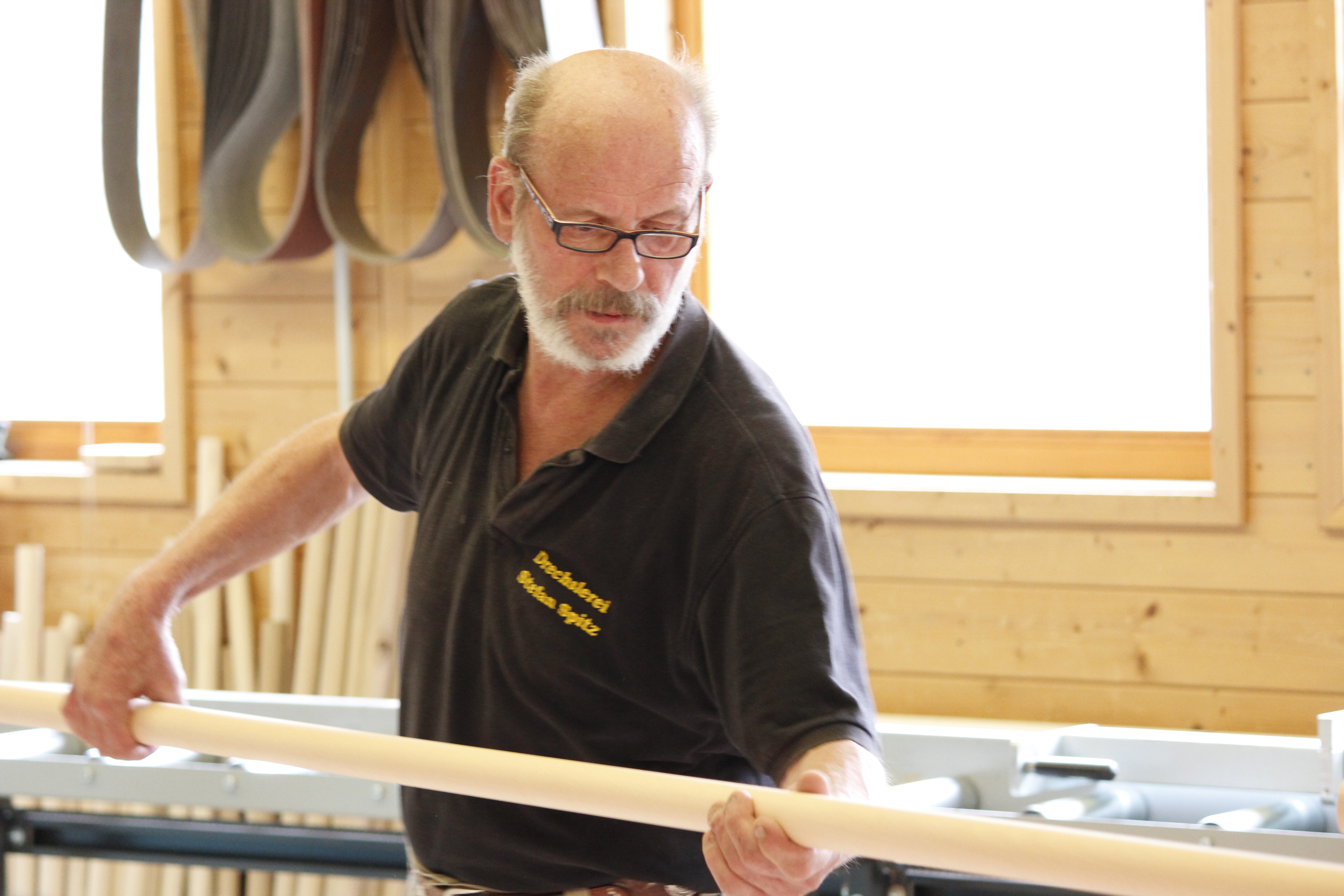Fabrication de mains courantes : un employé contrôle une main courante ronde en bois à l'atelier, mur en bois et établi