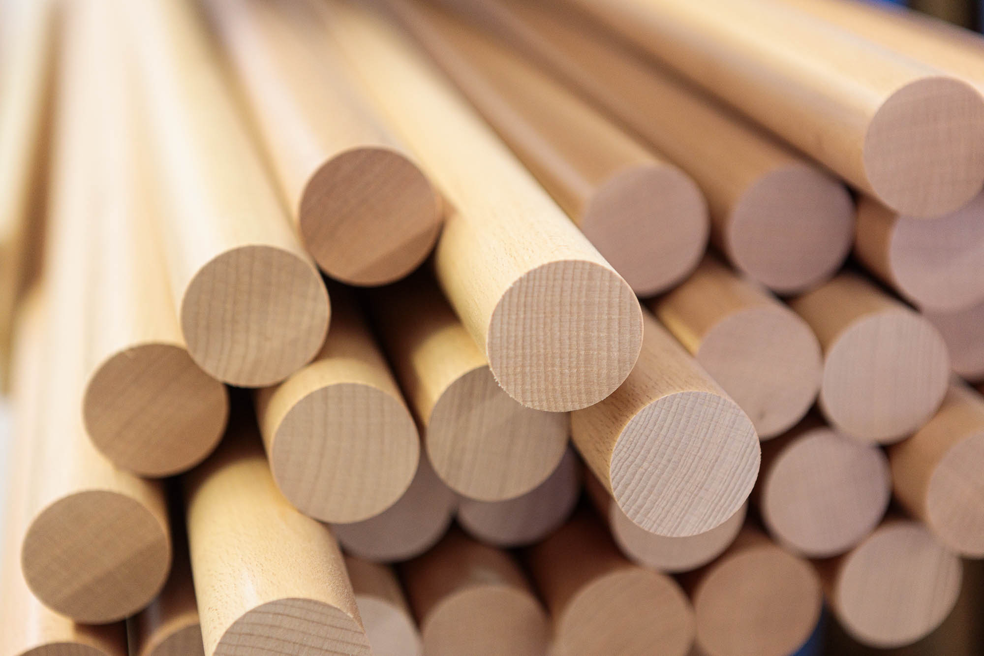 Mains courantes rondes en bois empilées, barres rondes claires aux abouts visibles à l'atelier, gros plan