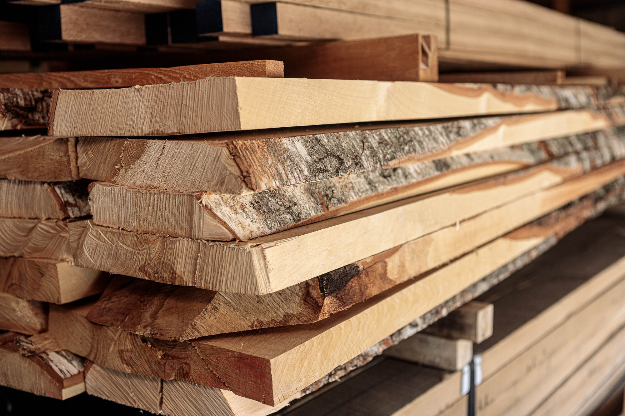 Stock de bois avec planches non délignées empilées, bois clair fraîchement scié avec écorce sur les rives, gros plan