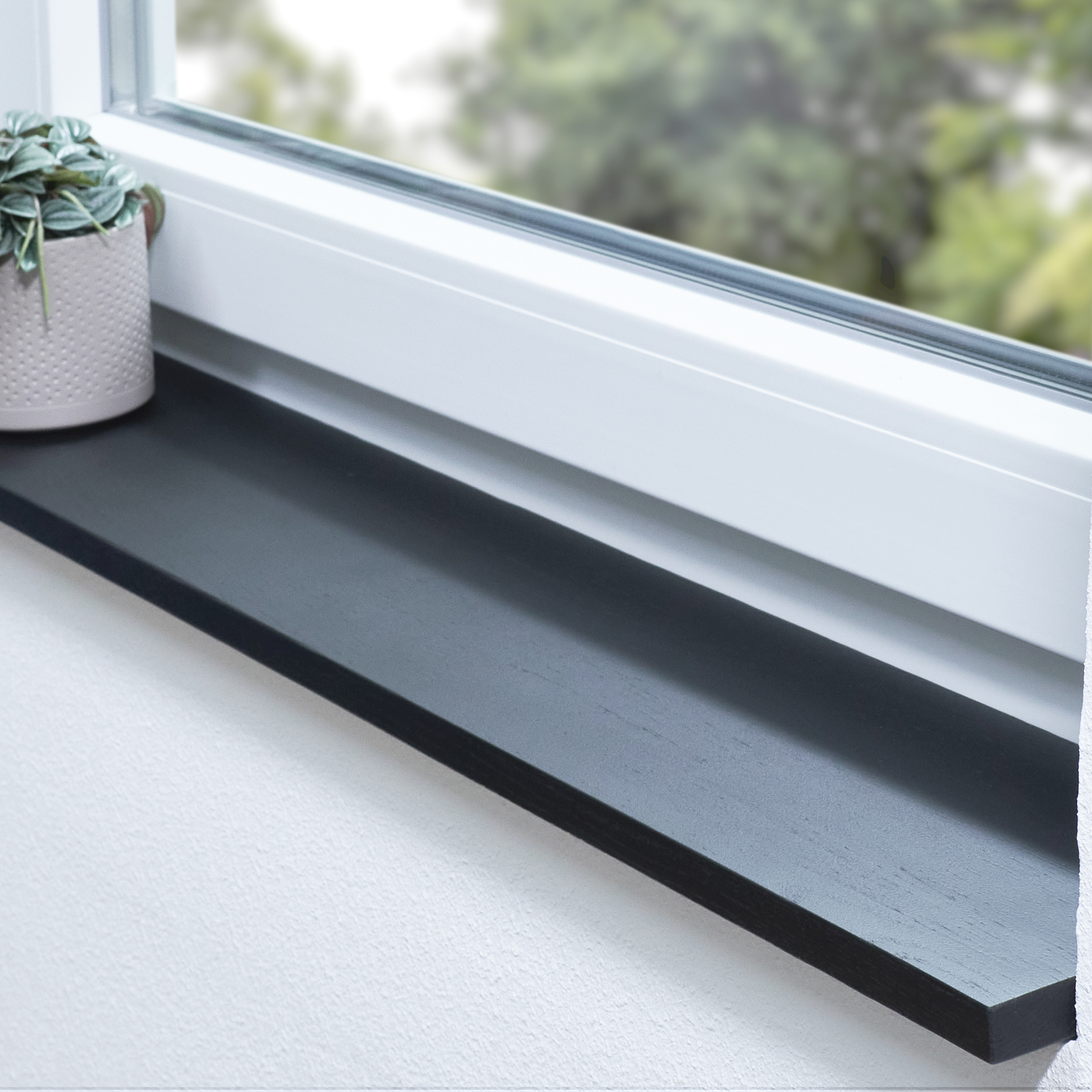 Appui de fenêtre en chêne teinté noir, abouté, dans une embrasure blanche avec plante en pot et vue sur la verdure