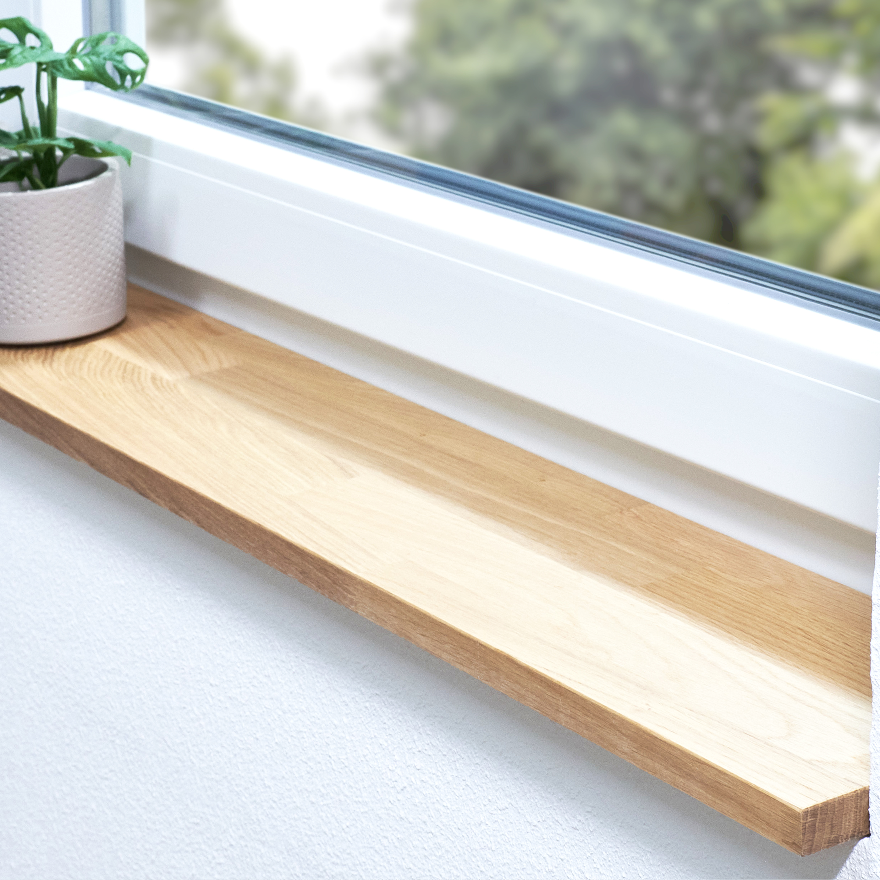 Appui de fenêtre en chêne naturel, abouté, dans une embrasure blanche avec plante en pot et vue sur la verdure
