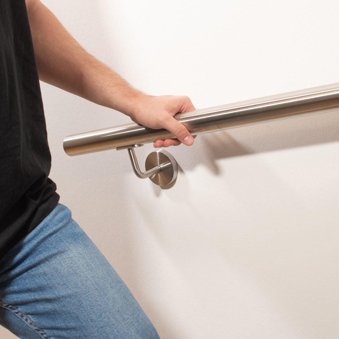 Main courante ronde en acier inoxydable sur mur blanc avec support inox, une personne en jean se tient à la main courante