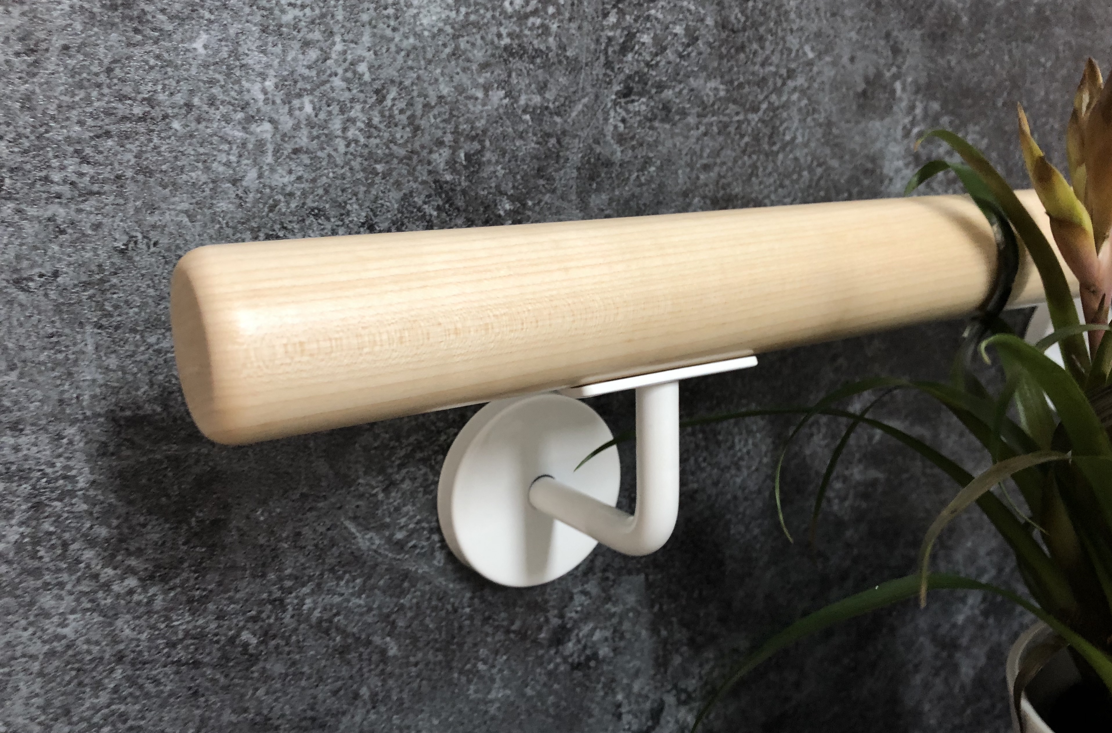 Main courante ronde en bois clair avec support de main courante laqué blanc sur mur en pierre gris foncé, plante verte