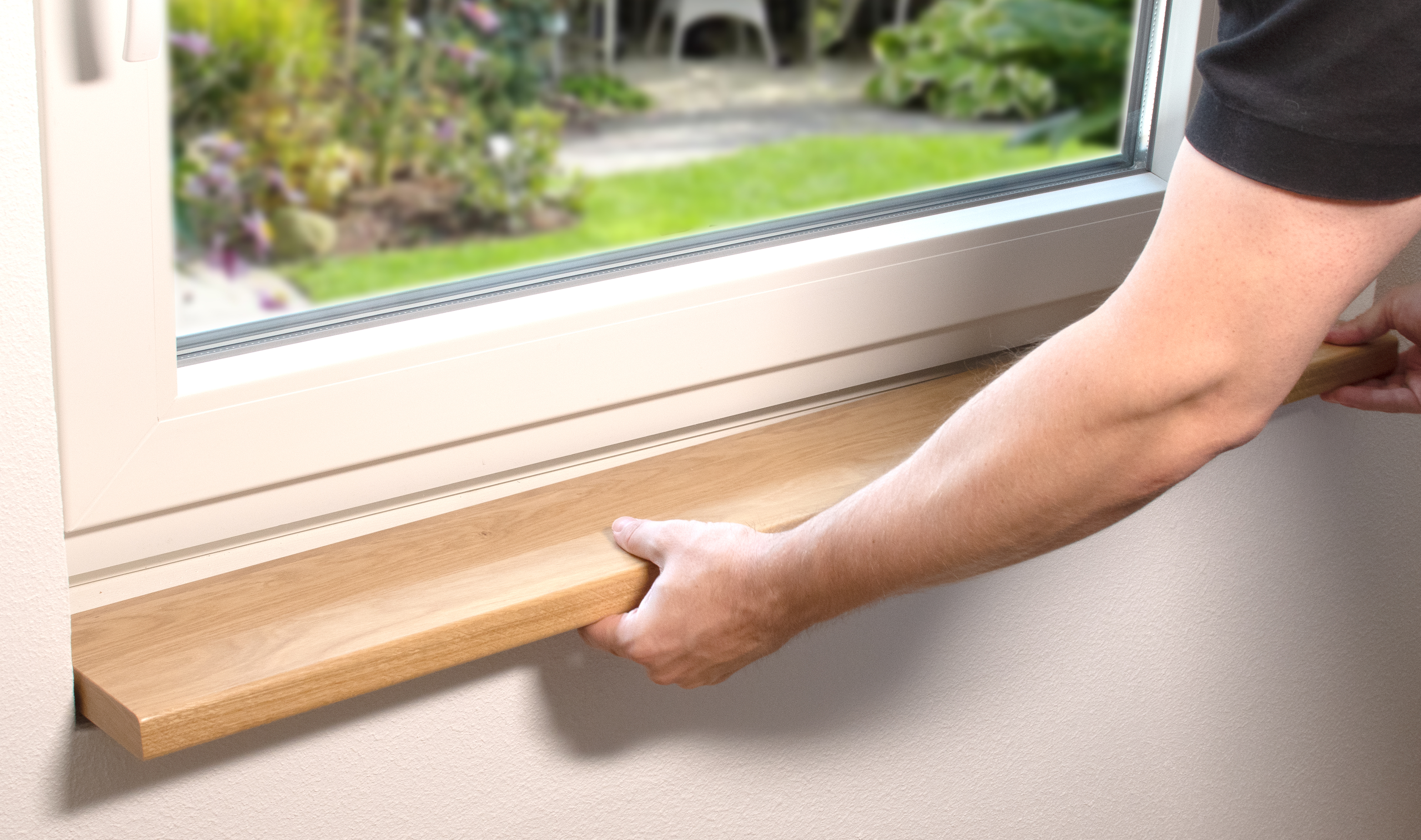 Appui de fenêtre en bois massif lors de la pose : une main place un appui clair sous une fenêtre blanche, vue sur le jardin