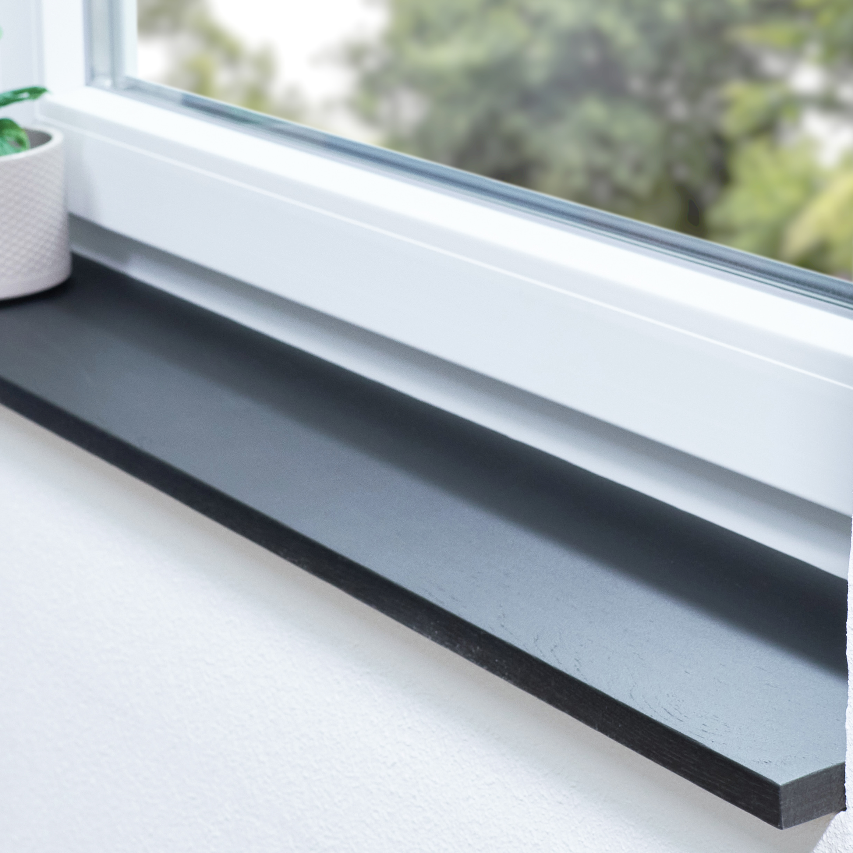 Appui de fenêtre en chêne teinté noir dans une embrasure blanche avec plante en pot et vue sur la verdure